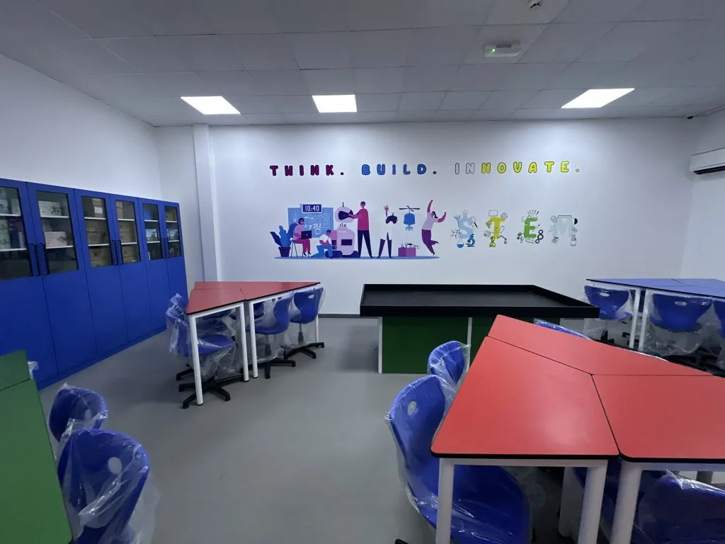 A school lab with blue storage cabinets along the wall, red and green group tables and blue chairs