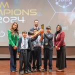 A winning student team and their coaches holding a trophy on stage at STEAM Champions UAE 2024