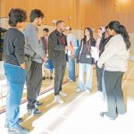 A coach briefing a group of student team members holding their project notes