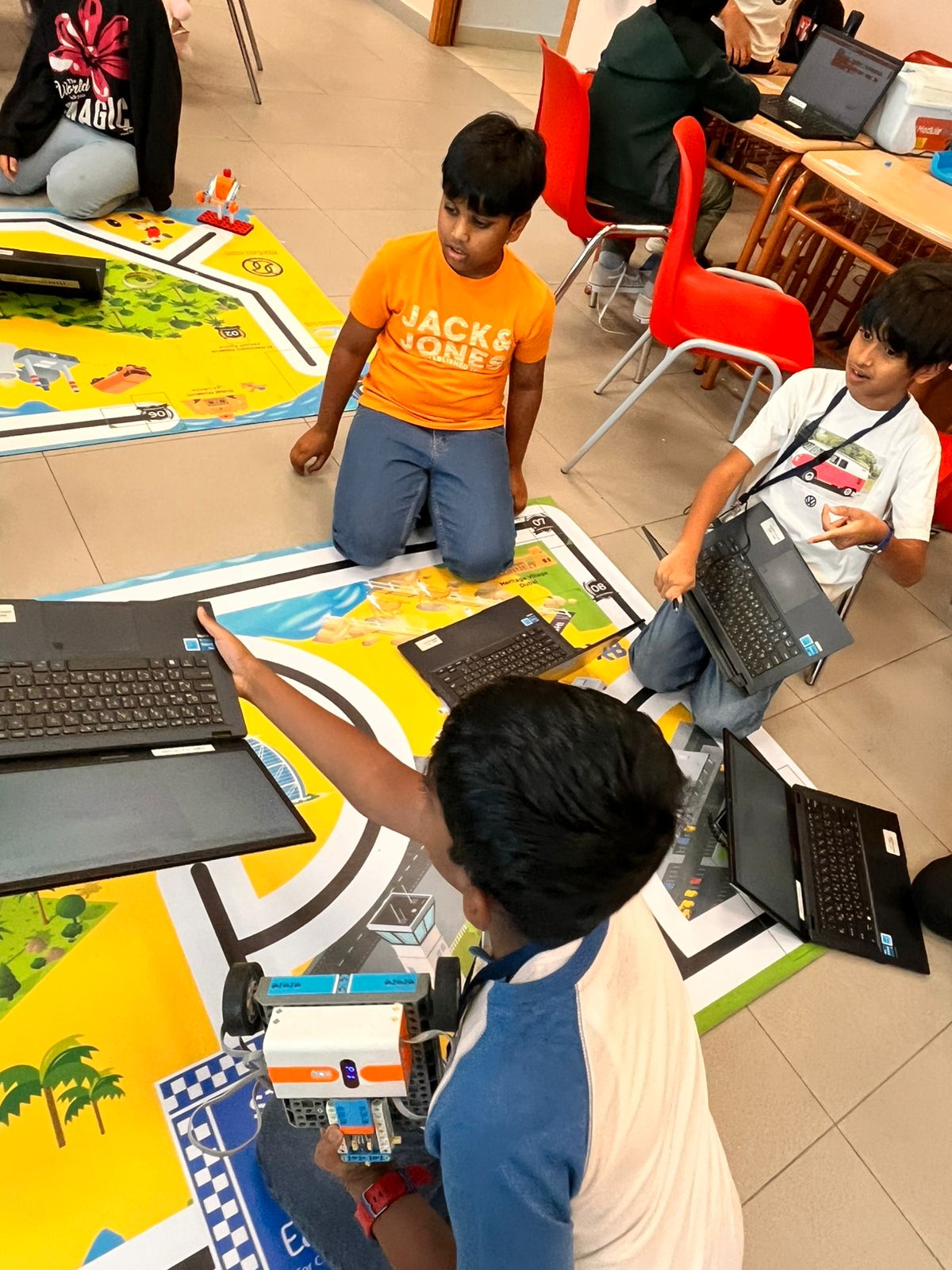 A student positioning a coded robot on an EduStream activity mat beside a laptop during a STEAM lesson