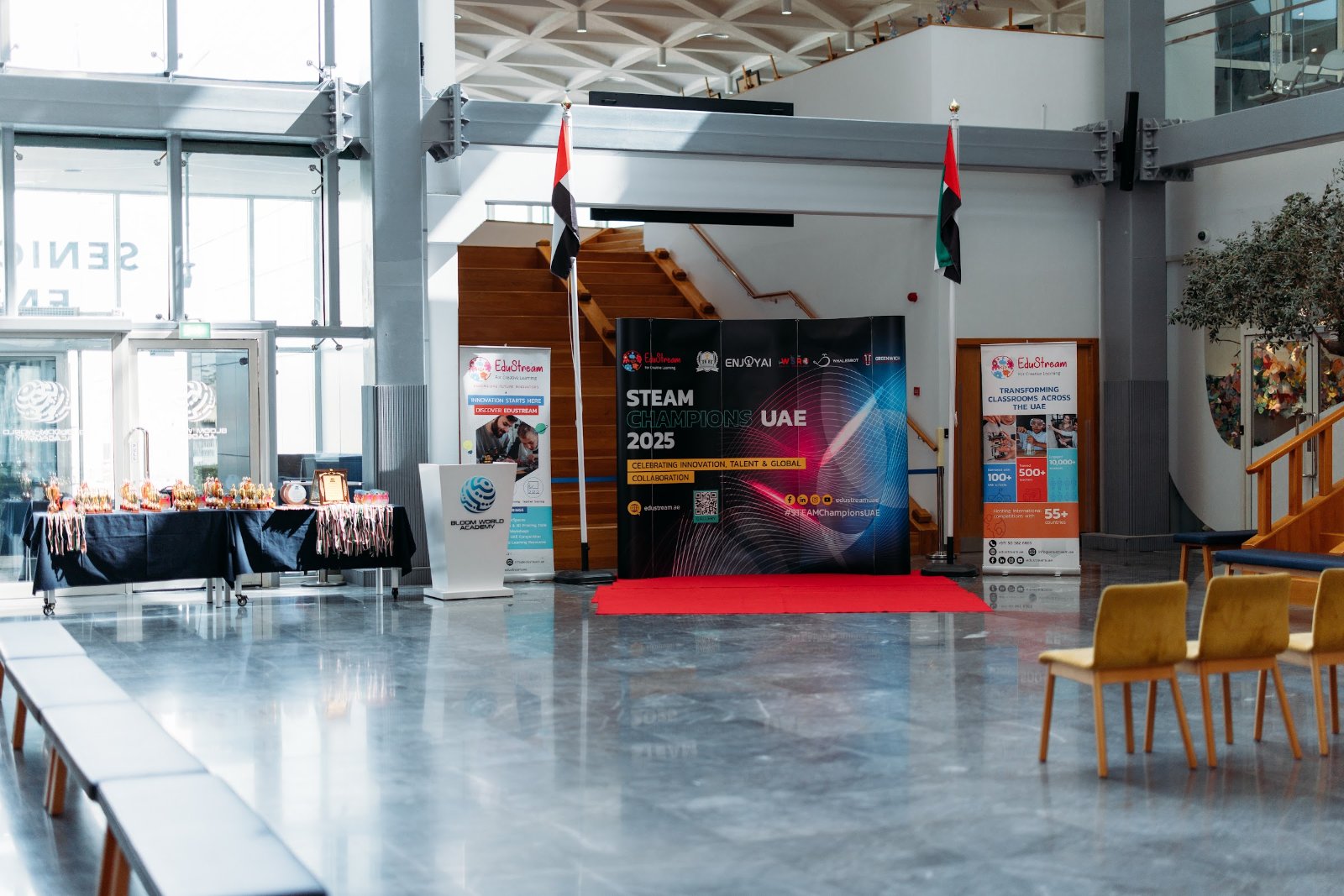 School atrium prepared for the STEAM UAE 2025 event, with an EduStream-branded stage backdrop, awards table and partner banners