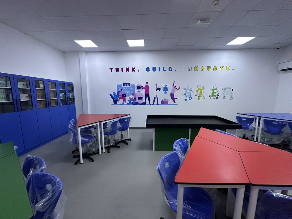 The completed RAK American Academy lab with red and green tables, blue storage cabinets and a Think. Build. Innovate. wall graphic