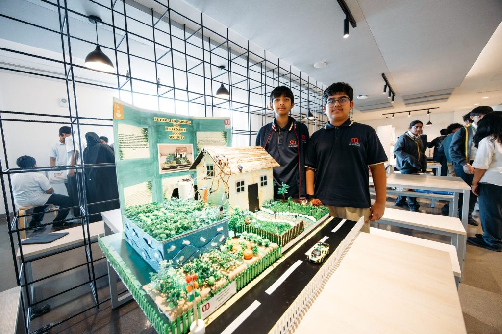 Two students standing beside their Automated Farming for Sustainable Food Security project model with a house, crops and a road