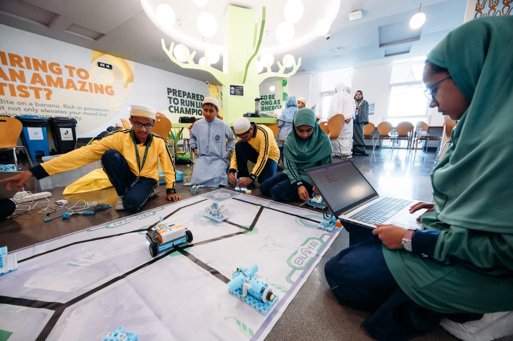 Students building and testing robots on a competition mat while a student programs on a laptop