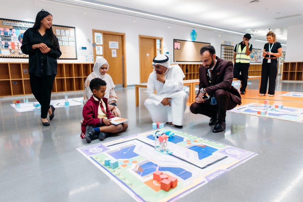 Adults crouching beside a young student who is working with a robot on a competition mat, while others look on