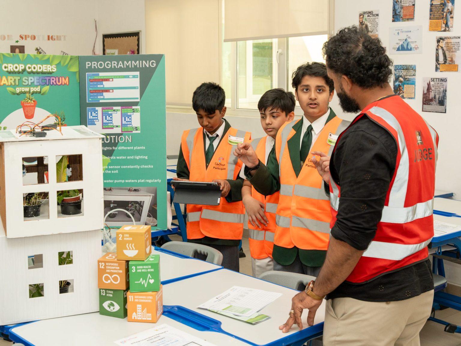 Students in high-visibility vests explaining their project to an adult wearing a vest marked Judge at the STEAM Champions UAE Nationals