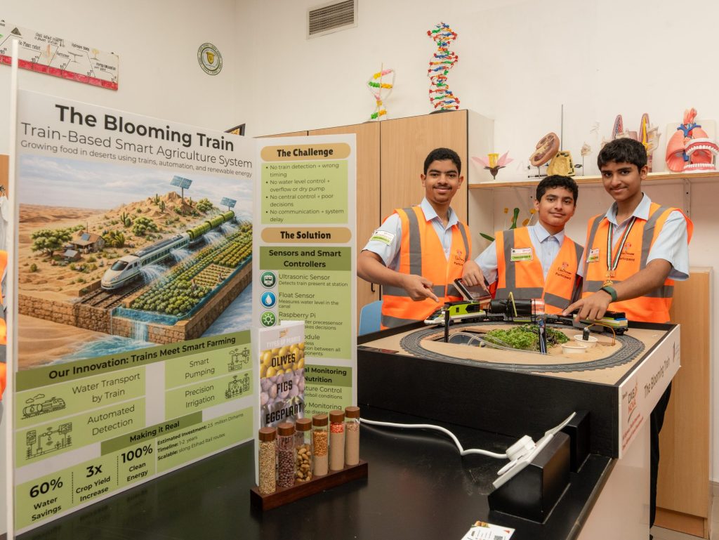 Three students in high-visibility vests beside their Blooming Train smart agriculture project display at the STEAM Champions UAE Nationals