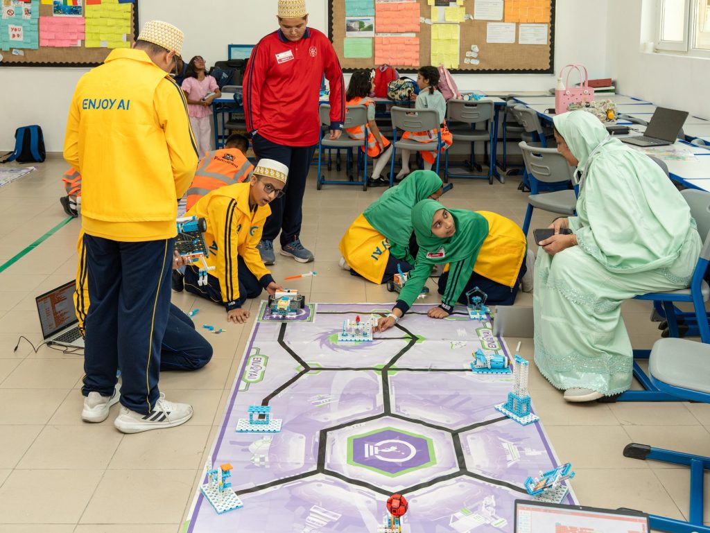 Students in team vests working on robots on a competition mat while adults look on, at the STEAM Champions UAE Nationals 2026