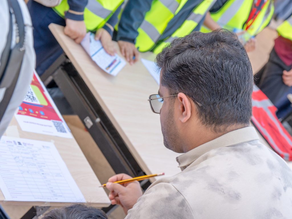 An adult recording scores on a printed sheet with a pencil while students in vests stand nearby